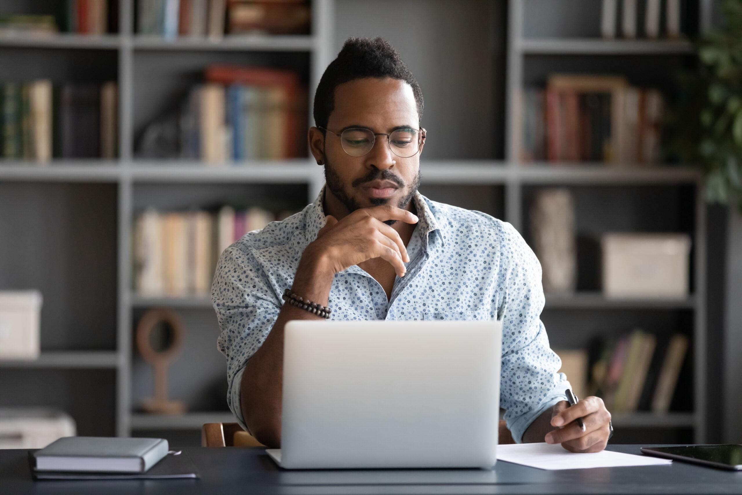 Thoughtful African American businessman looking at laptop screen, touching chin